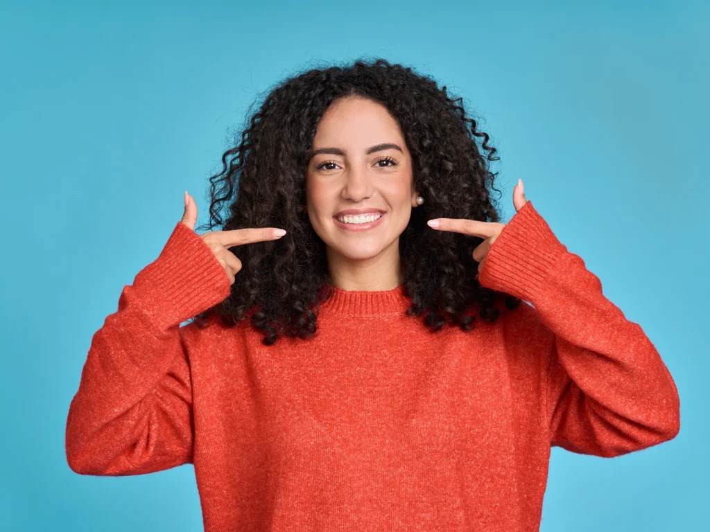 Young woman smiling and pointing to her clean, white teeth after a teeth cleaning in Bartow, FL at Bartow Dental Arts